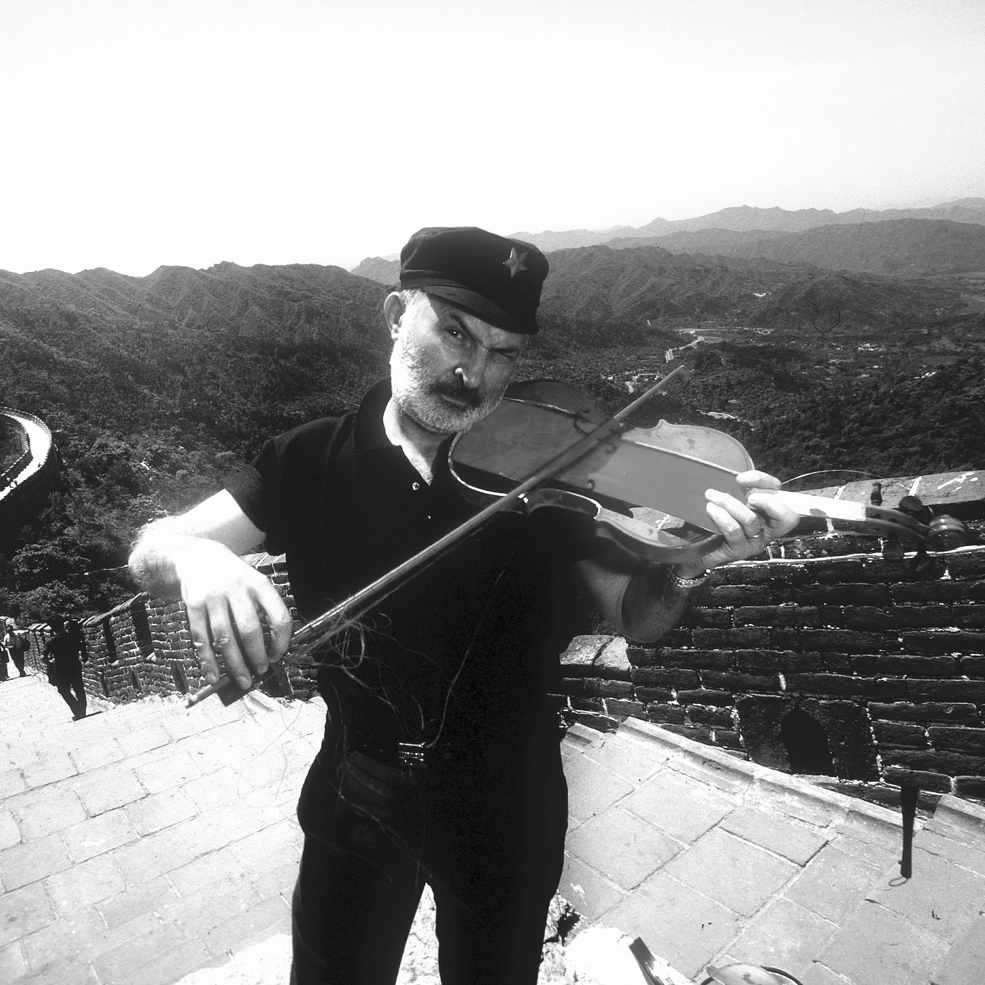 Arman sur la Grande Muraille de Chine, mimant un geste de violon.