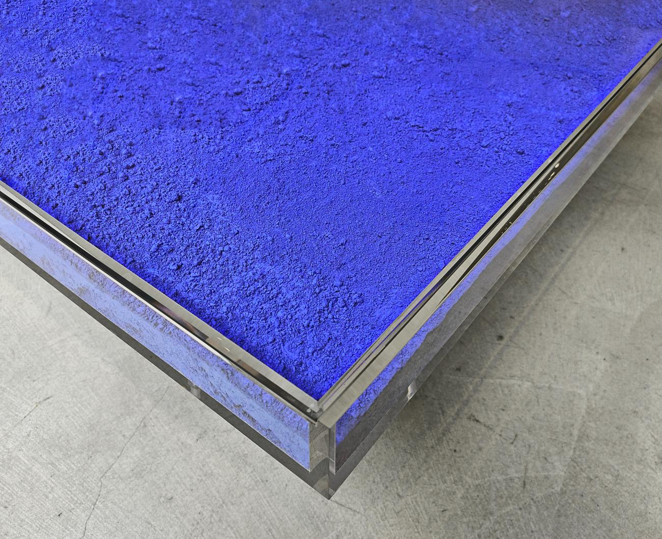Détail d’angle de la table IKB® d’Yves Klein : pigment bleu IKB® à la texture poudreuse, structure en plexiglas transparent sur sol en béton brut.