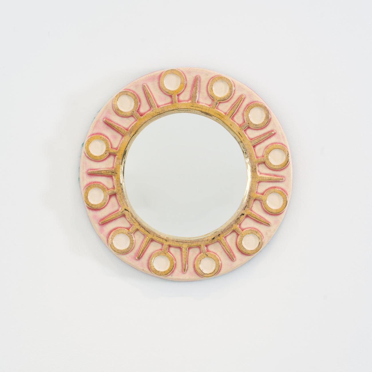 Miroir mural rond en céramique émaillée rose pâle et or de Mithé Espelt, modèle « Soleil ». Décor graphique stylisé aux motifs circulaires évoquant le rayonnement solaire, réalisé à la main dans les années 1950.
