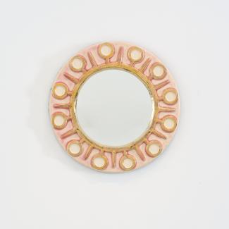 Miroir mural rond en céramique émaillée rose pâle et or de Mithé Espelt, modèle « Soleil ». Décor graphique stylisé aux motifs circulaires évoquant le rayonnement solaire, réalisé à la main dans les années 1950.